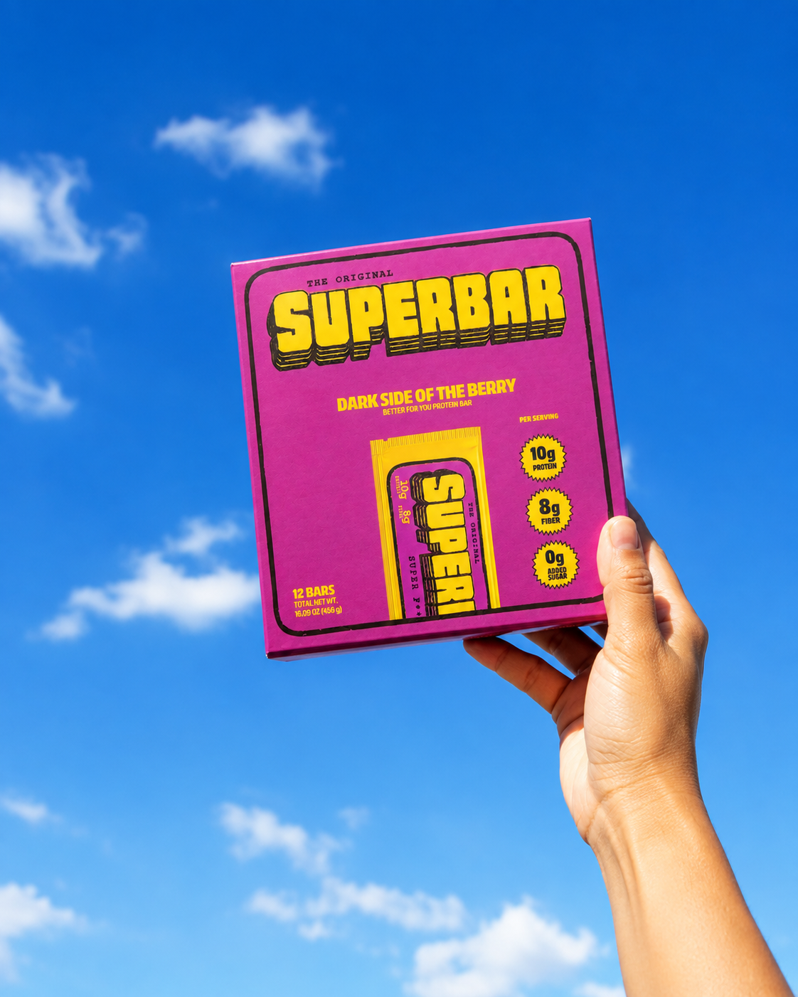 Hand holding a Superbar box against a blue sky